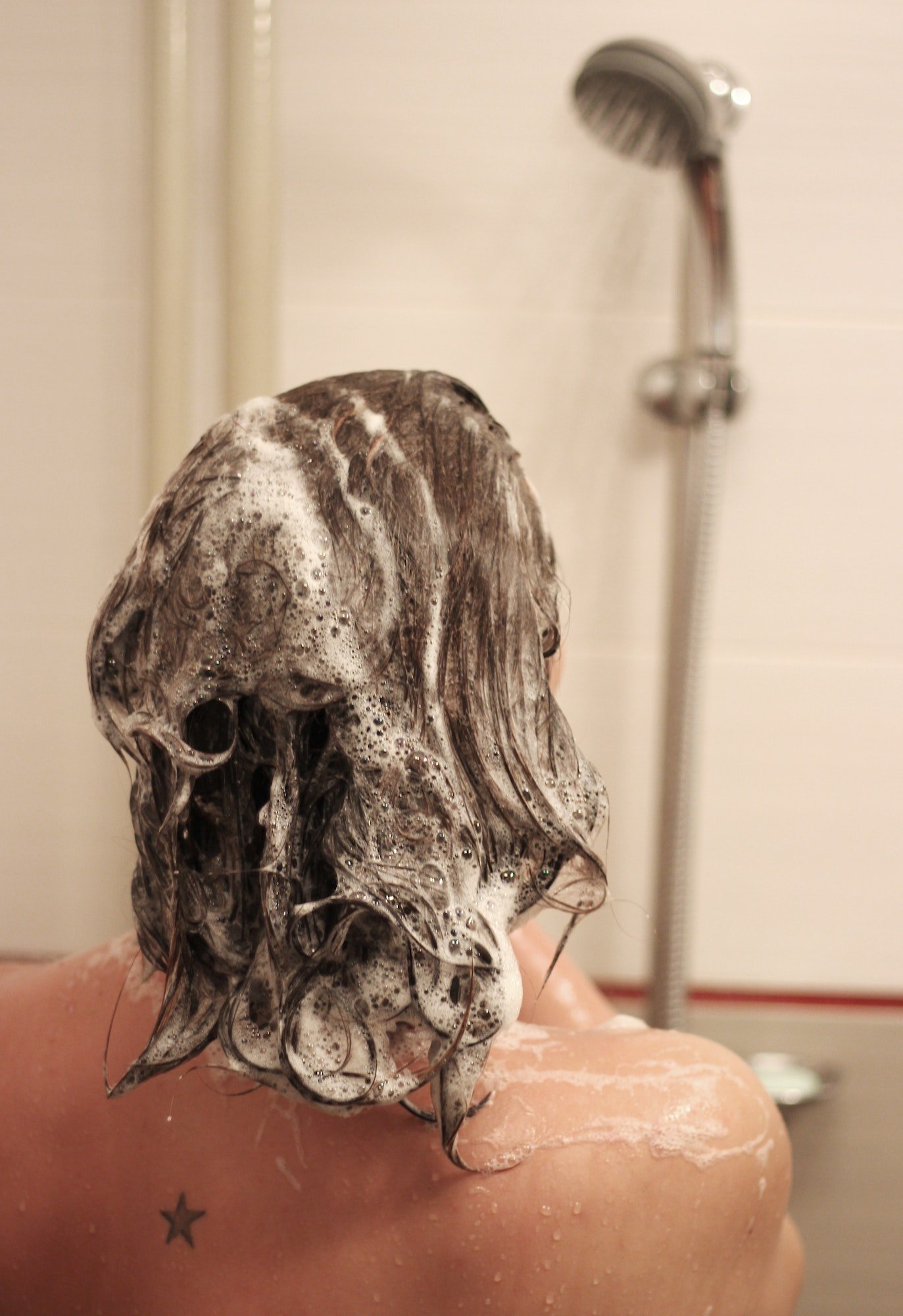 En ung kvinne i dusjen med shampoo i håret. 