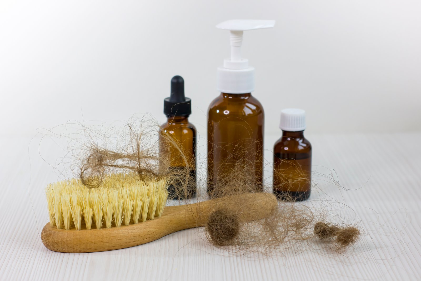 Medication bottles and hairbrush on white wooden table. Hair loss problem.