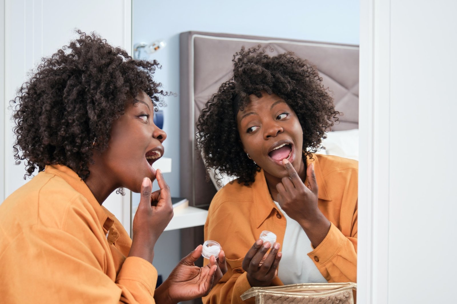 Happy african woman applying vaseline in her bedroom.